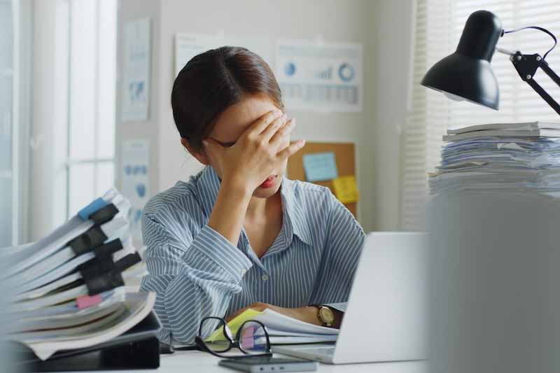 Woman sitting at desk, holding her head in pain.